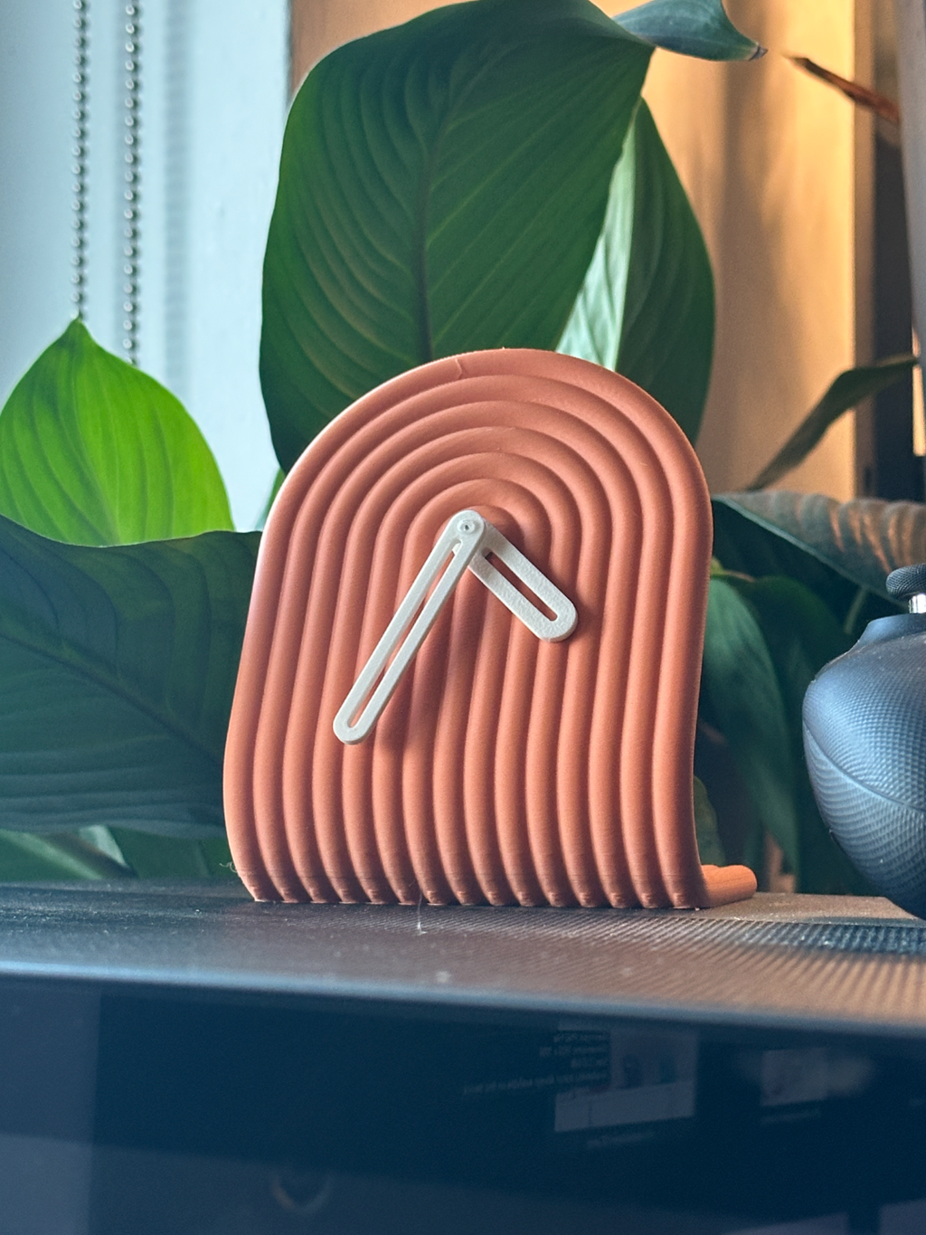 3D printed clock on a surface with green leaves in the background