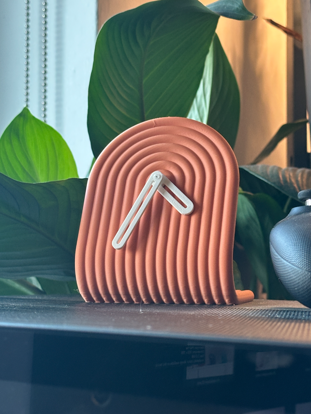 3D printed clock on a surface with green leaves in the background